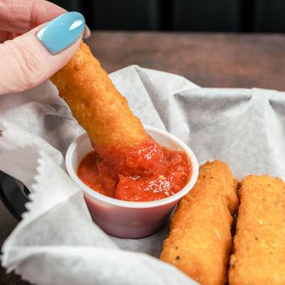 Hand dipping a mozzarella stick into marinara sauce.