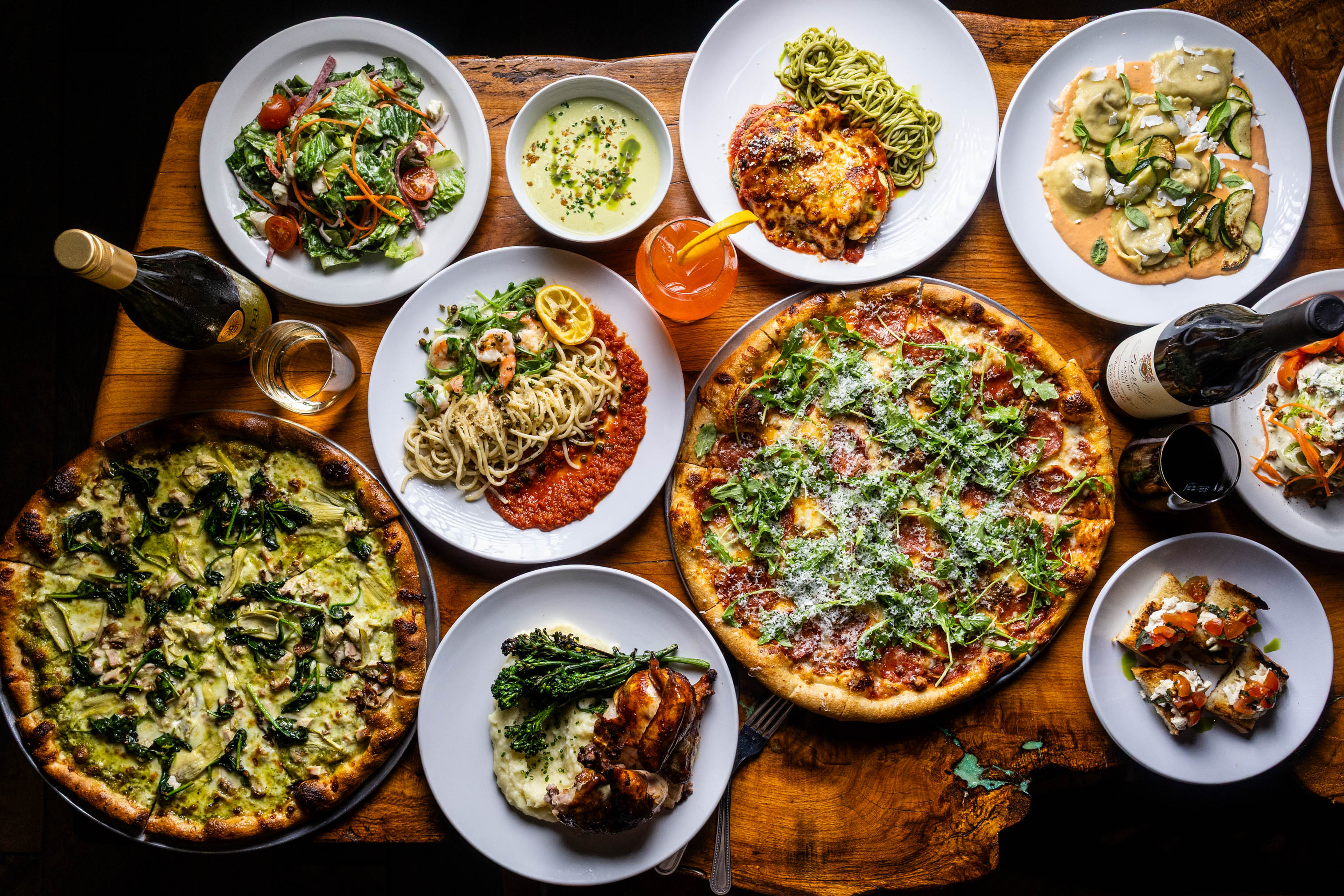 A spread of dishes such as pizzas, pasta dishes, salads, and a drink