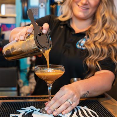 A bartender pouring espresso martini into a glass from a shaker.