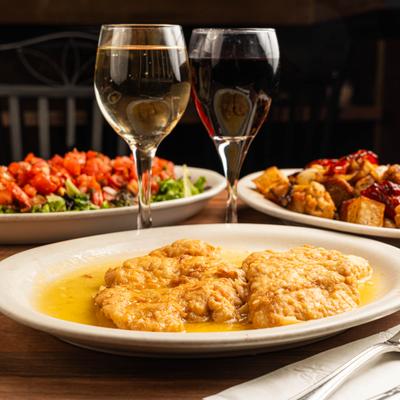 Chicken Francese plate, accompanied with two glasses of wine and two other dishes.