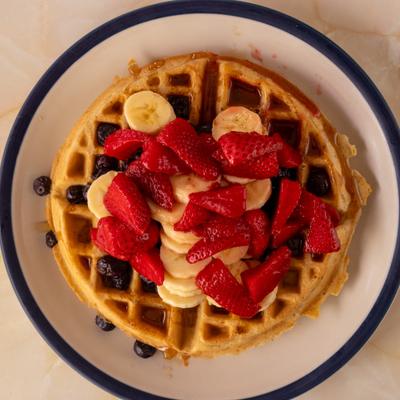 Waffle topped with fresh fruit, served on a white plate with a blue rim.
