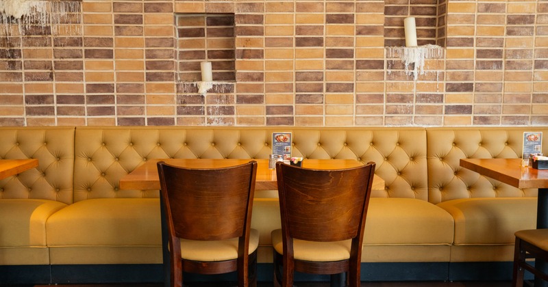 Interior, mustard bench seating, wooden chairs, brick wall, and candles on shelves