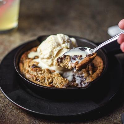 Skillet Cookies topped with ice cream, a hand holding a spoonful.