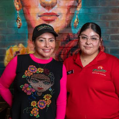 Two staff members posing in front of mural.