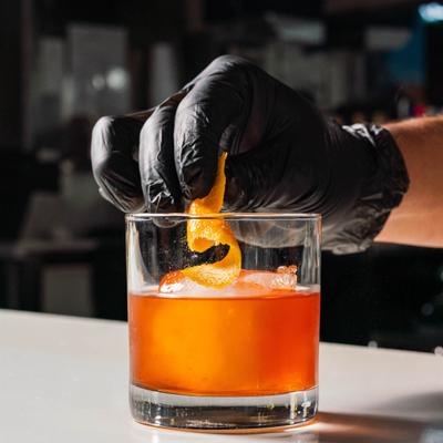 Bartender garnished Old fashioned cocktail with orange peel.