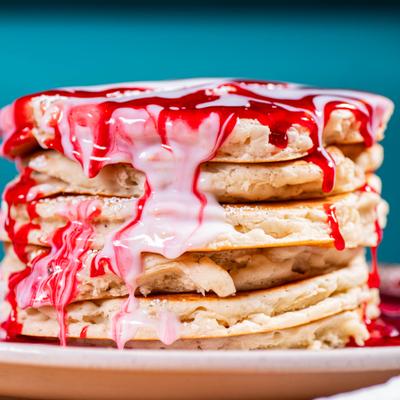 Tall pancake stack with dripping strawberry and cream sauce.