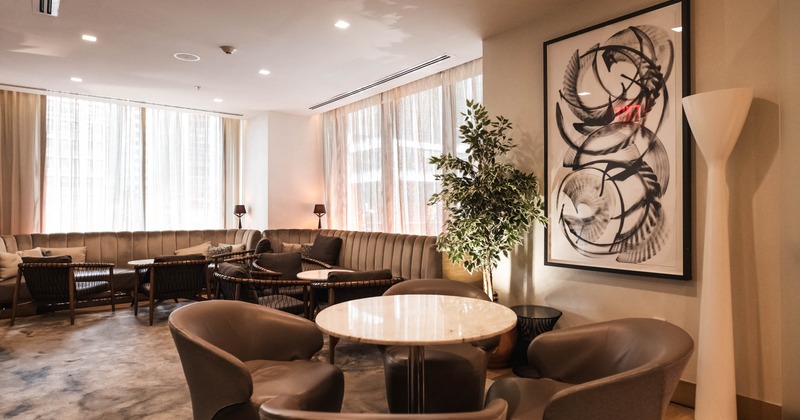 A modern lounge with plush chairs around a marble table, a curved sofa by large windows