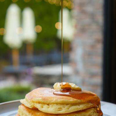Fluffy pancakes with a pat of butter being drizzled with syrup.