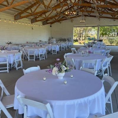Large indoor event space with numerous tables, featuring white linens and floral centerpieces.