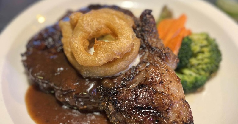 Close-up of a grilled steak topped with onion rings and gravy