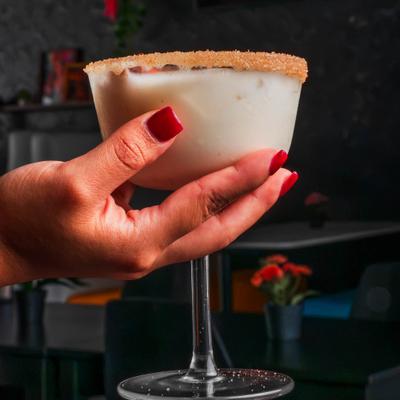 A hand holding a horchata martini with a cinnamon-sugar rim.