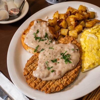 Country fried steak topped with gravy, served with scrambled eggs and potatoes.