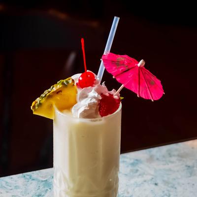 Pina colada garnished with pineapple wedge, cherries, cream, straw and pink umbrella.