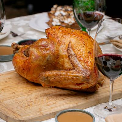 Roasted turkey on a wooden board, surrounded by glasses of red wine and plates of food.