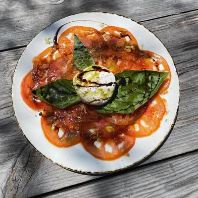 A plate of burrata caprese served on an outdoor table.