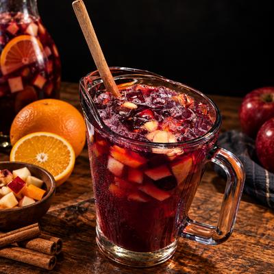Red sangria in a glass pitcher, surrounded by fresh fruit and cinnamon sticks.