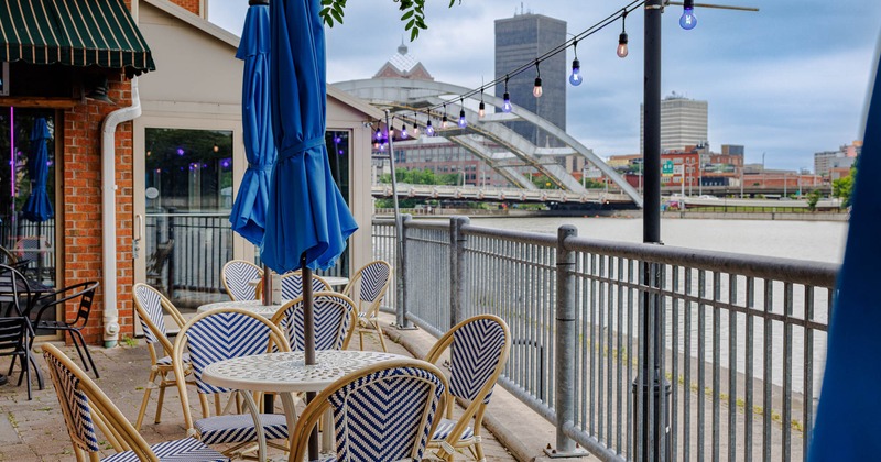 Exterior, seating area, round tables for four, stone paving, metal railing, river view