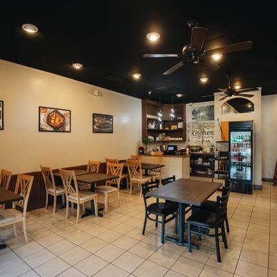 Interior featuring a black ceiling, tilled flor, table seating, small counter and framed images of food.
