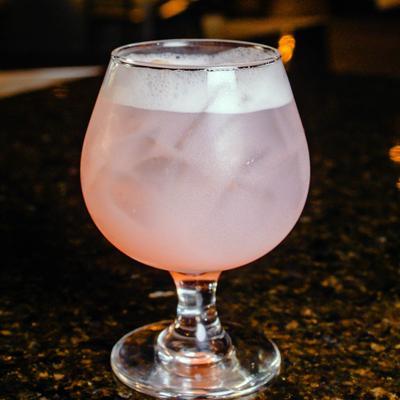 A pink Lychee Martini cocktail served in a snifter-style glass on a dark granite bar top.