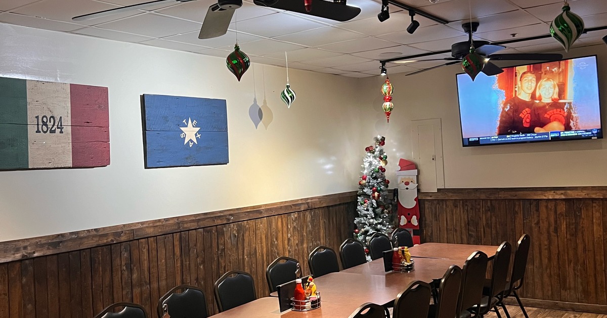 A room featuring a television and a table surrounded by chairs, decorated for Christmas