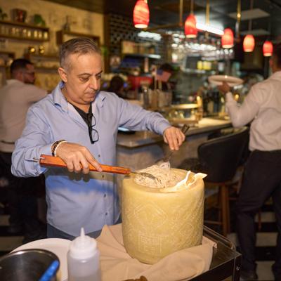 A server mixing pasta inside a large cheese wheel.