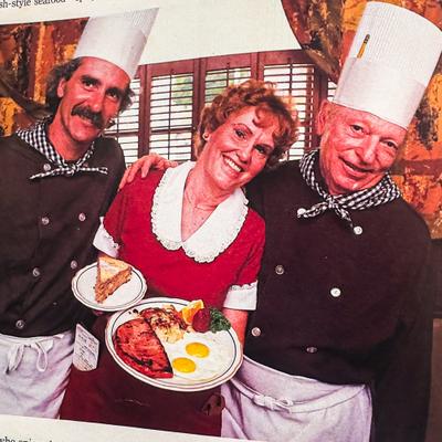 Two chefs with a server holding plates of food