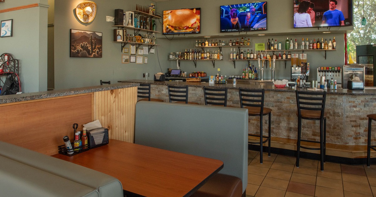 Restaurant interior featuring a bar area with liquor bottles, three mounted TVs