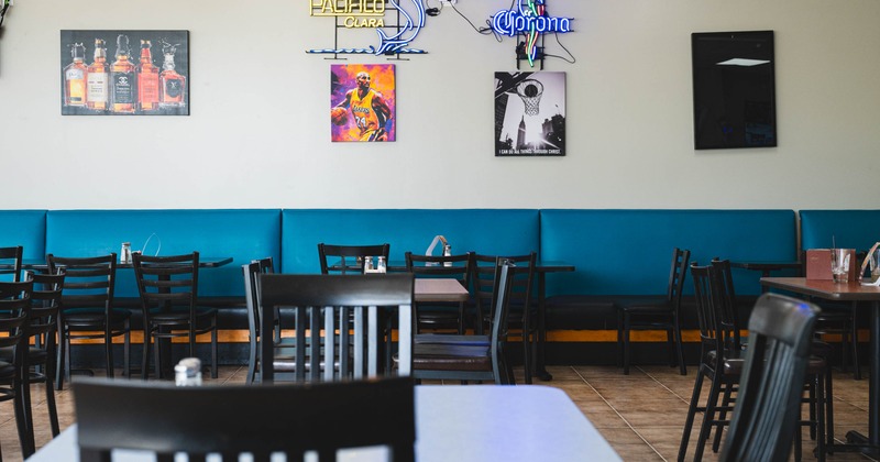 Interior with tables and chairs, turquoise bench seating and neon signs on the wall.