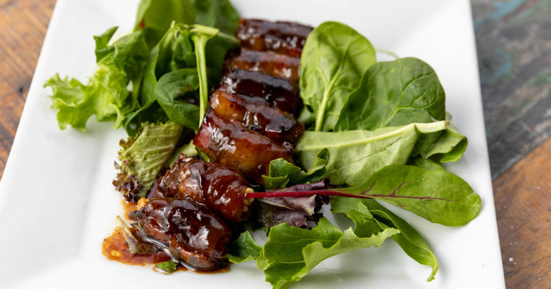 Fried large bacon wrapped dates served on spinach leaves