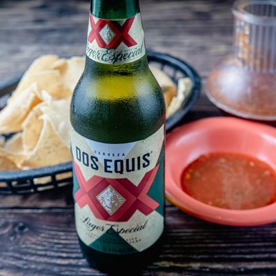 Bottle of beer with chips and dip served on a table.