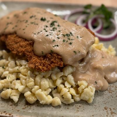 Breaded chicken schnitzel topped with gravy, served over small pasta.