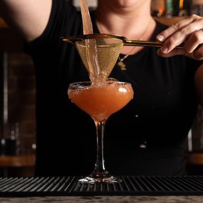 Bartender straining cocktail into a coupe glass.