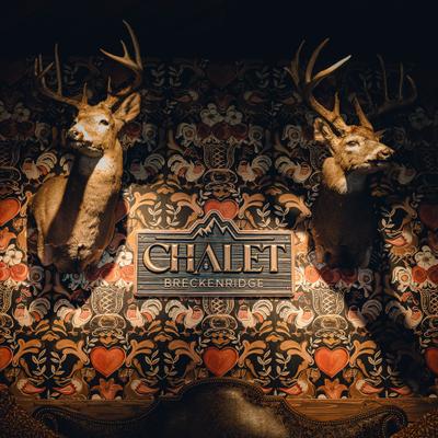 Two deer heads are mounted on a patterned wall with Chalet Breckenridge sign.