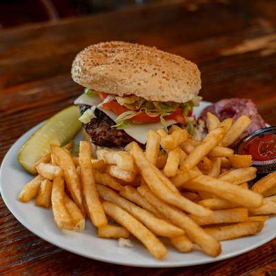 Burger and fries served with a pickle and sauce on a white plate.