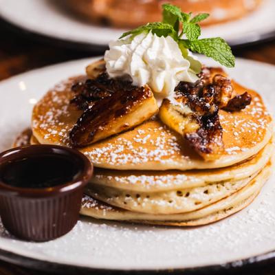 Fluffy pancakes topped with caramelized bananas, toasted nuts, whipped cream, and mint.