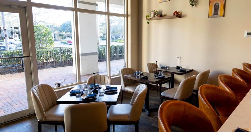 A cozy dining area with tables, beige chairs, large windows, a bar counter with orange-brown chairs