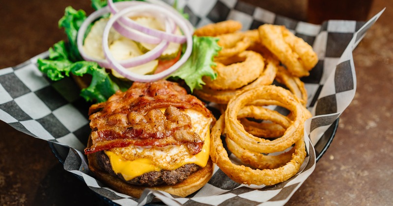 Burger topped with cheese, fried egg and bacon, served with onion rings