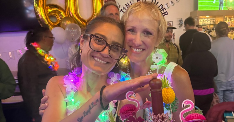 Two people posing together at a gathering decorated with leis and party items