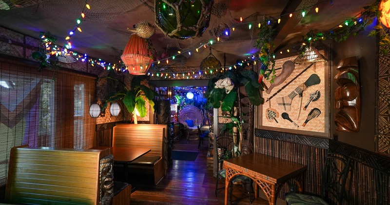 A cozy, dimly lit tiki bar with wooden booths and tropical decor
