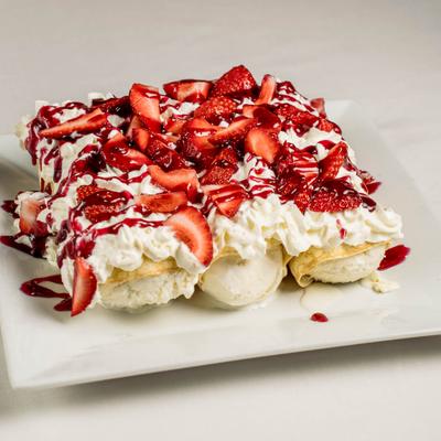 Three crepes with vanilla ice cream filling topped with fresh strawberries, sauce and whipped cream.