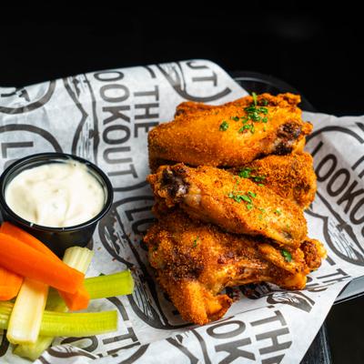 Chicken wings are garnished with fresh parsley, served with vegetable sticks and a dip.