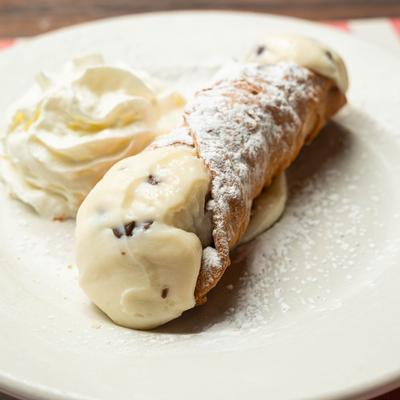 A cannoli served on a white plate with whipped cream on the side.