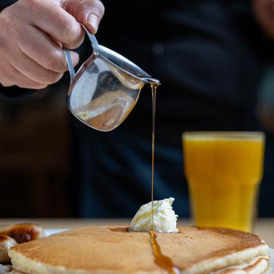 Syrup being poured over the pancake topped with butter.