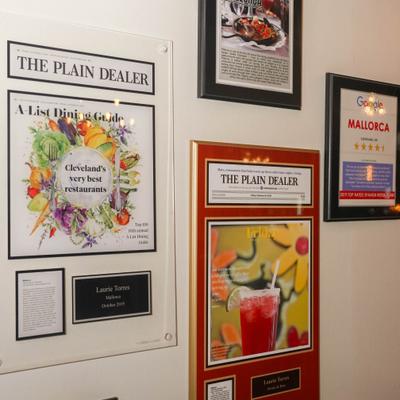 Wall with framed articles and restaurant recognition plaques.