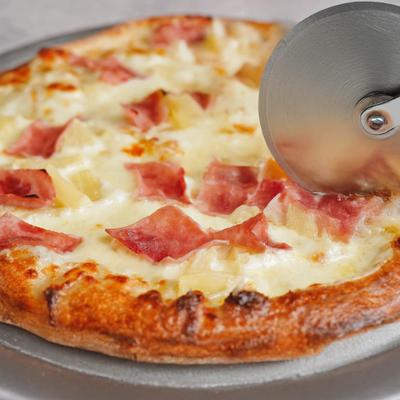 Hawaiian Pizza being sliced, close-up.