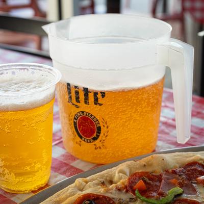 A pitcher and a cup of cold beer beside a pizza topped with pepperoni.
