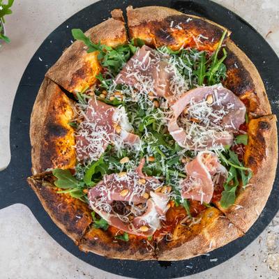 Prosciutto pizza topped with arugula and shaved cheese, top view.
