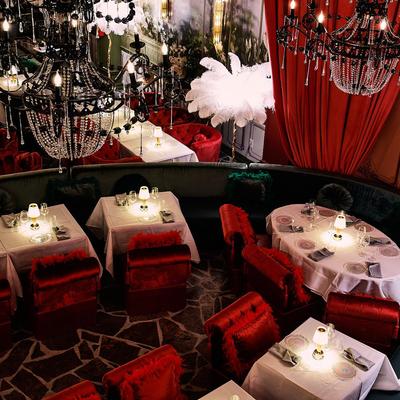 Interior with tables and chairs, red velvet curtains and elaborate chandeliers.