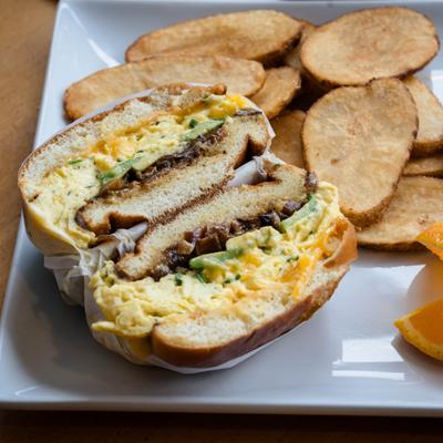 Breakfast sandwich with scrambled eggs, breaded protein, and a side of potato chops.