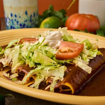 Close-up of enchiladas covered in mole sauce and salad.